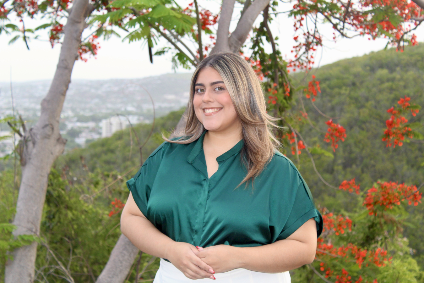 Ana Torres standing outside with mountains and red tree blooms in the background.