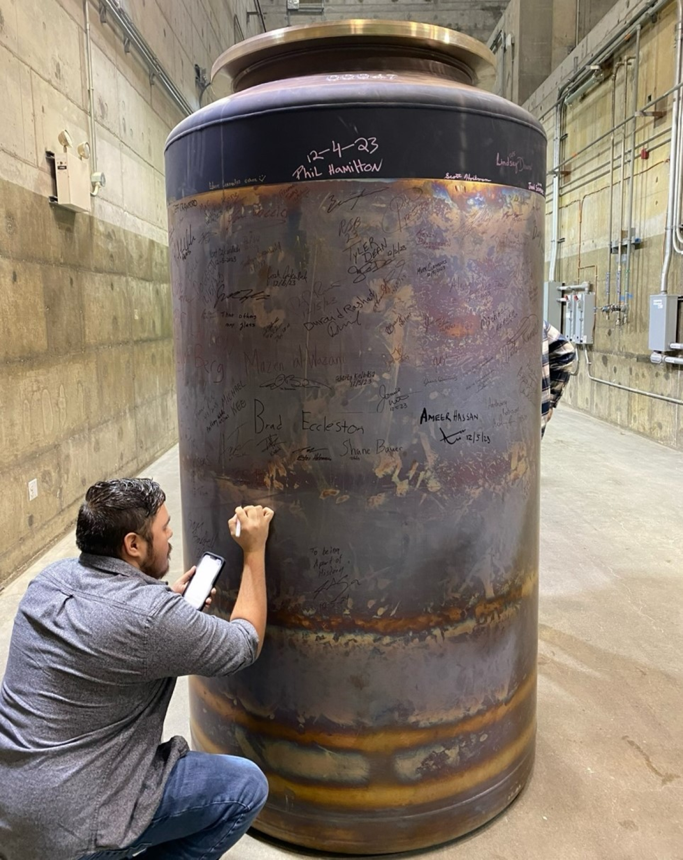 Kevin Estala Rodriguez crouching and writing on a large metal cylinder