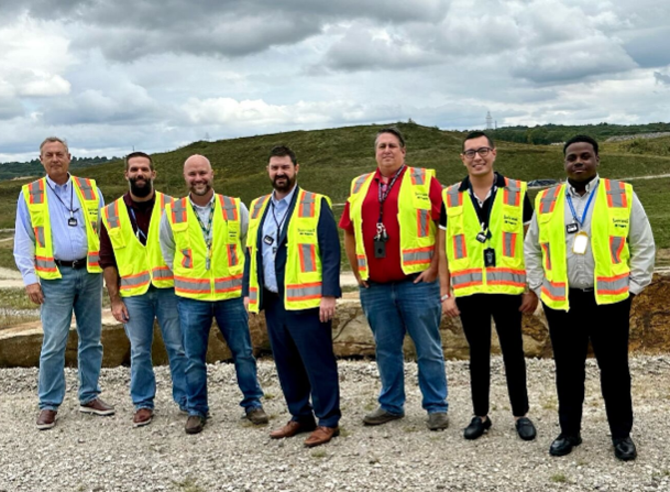 Group of 7 men wearing neon safety vests standing outside.