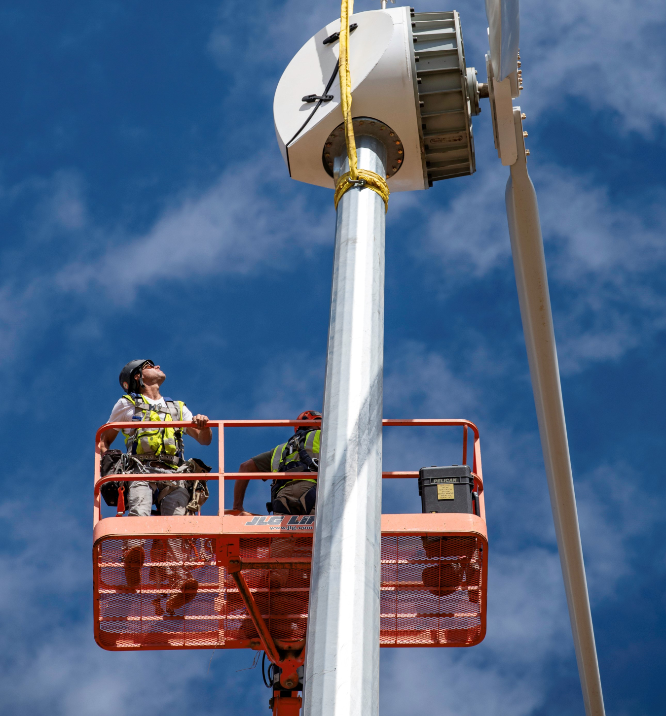 A worker is hoisted by a lever to the top of a wind turbine. 