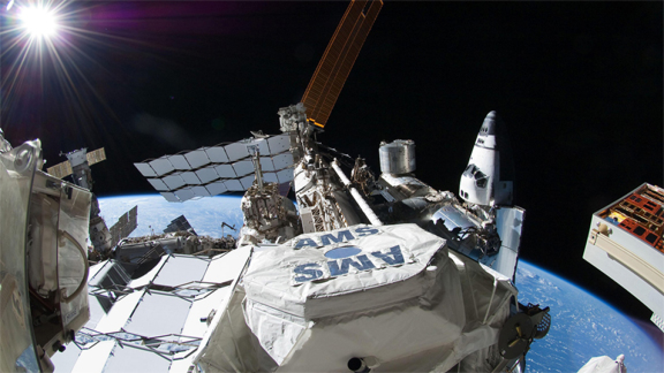 Pictured here, the AMS is visible on the ISS just after being installed, with a US Space Shuttle docked on the far right, a Russian Soyuz capsule docked on the far left, and the blue Earth that houses all nations visible across the background.