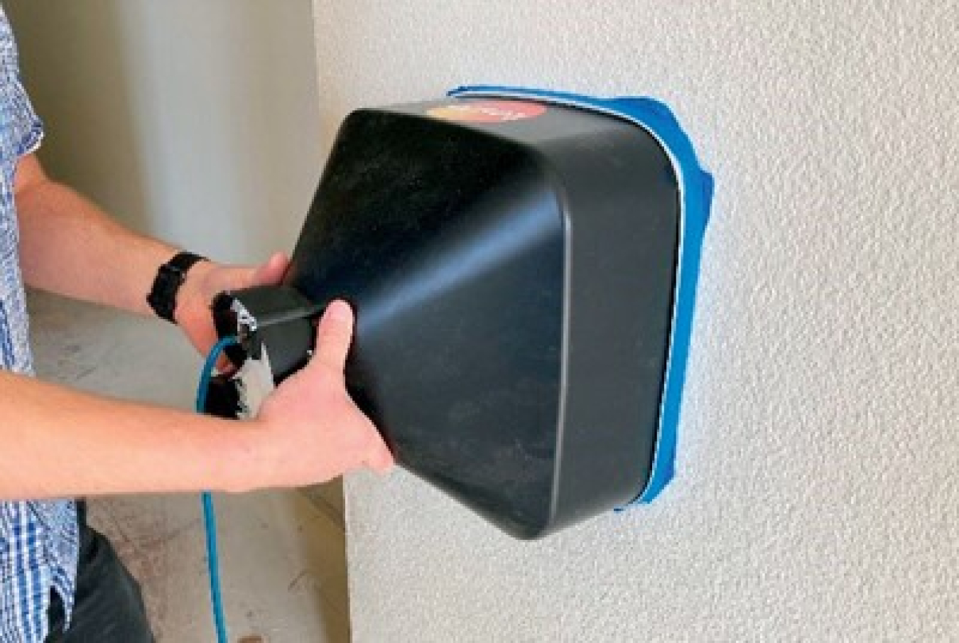 Person holds machine up to wall inside house to measure air flow