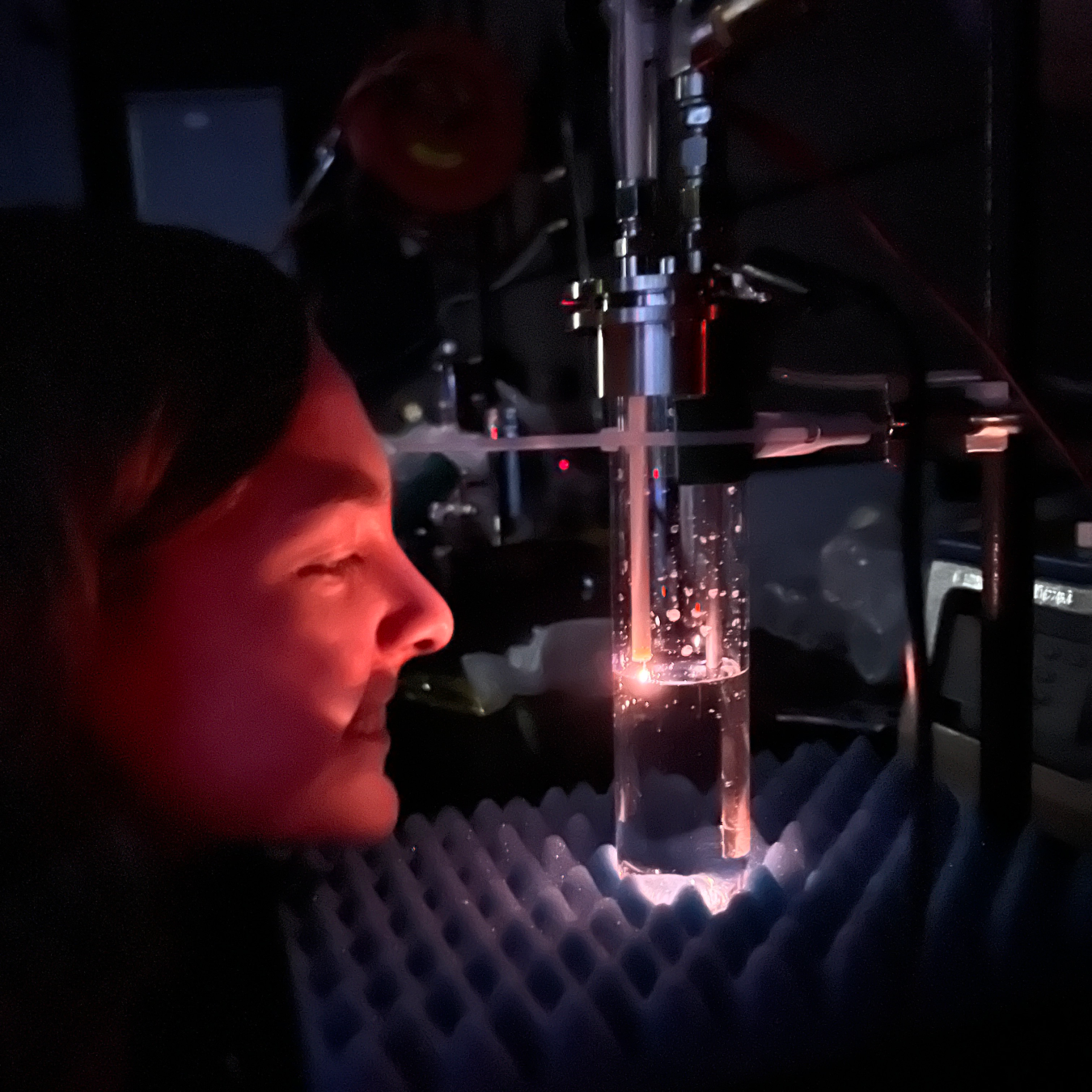 A person's face is illuminated by a science experiment with a glowing tube