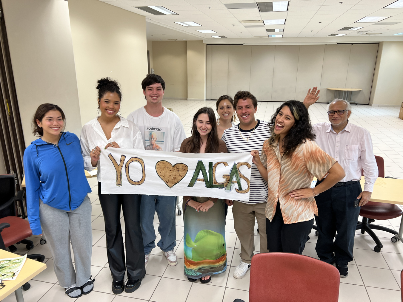 Students proudly display their banner reading 'Yo Algas' (I love algae), painted with pigments from different strains of algae and seaweed. The banner, created during a workshop, highlights the practical use of algae products.