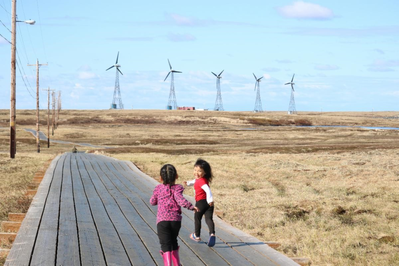 Children play on a path with wind turbines in the background.