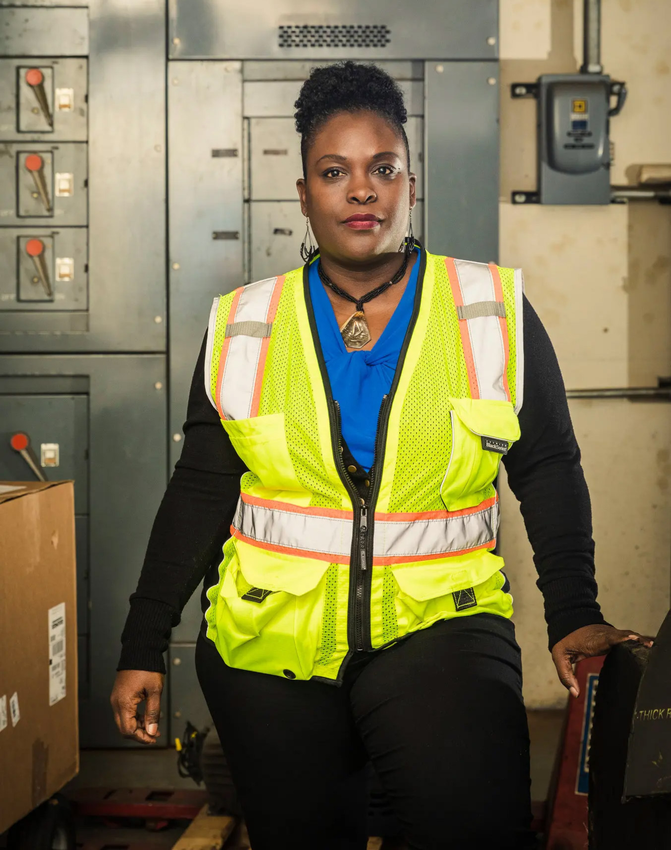 A woman in front of electrical equipment wearing a safety vest