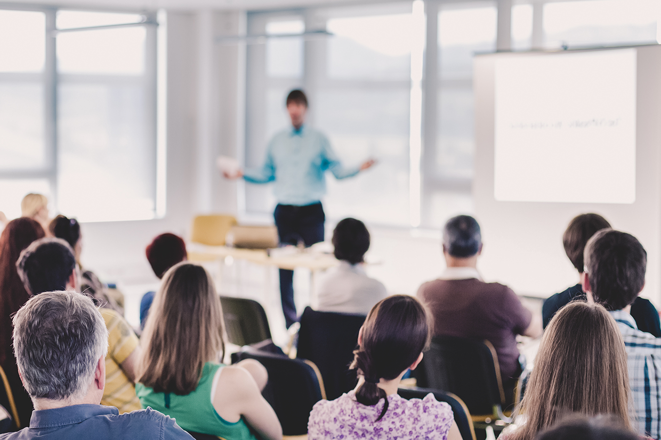 A person in front of a screen giving a presentation to an audience of people