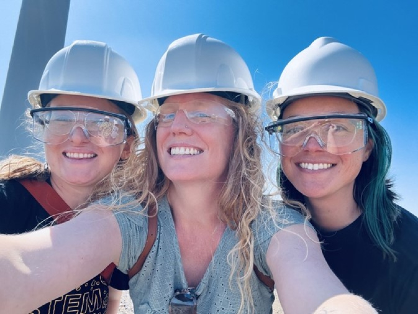 Three people are standing wearing helmets for work