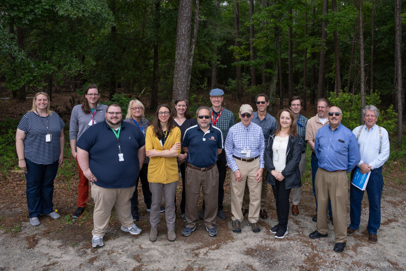 A large group of people stand outside in front of trees and pose for a group picture