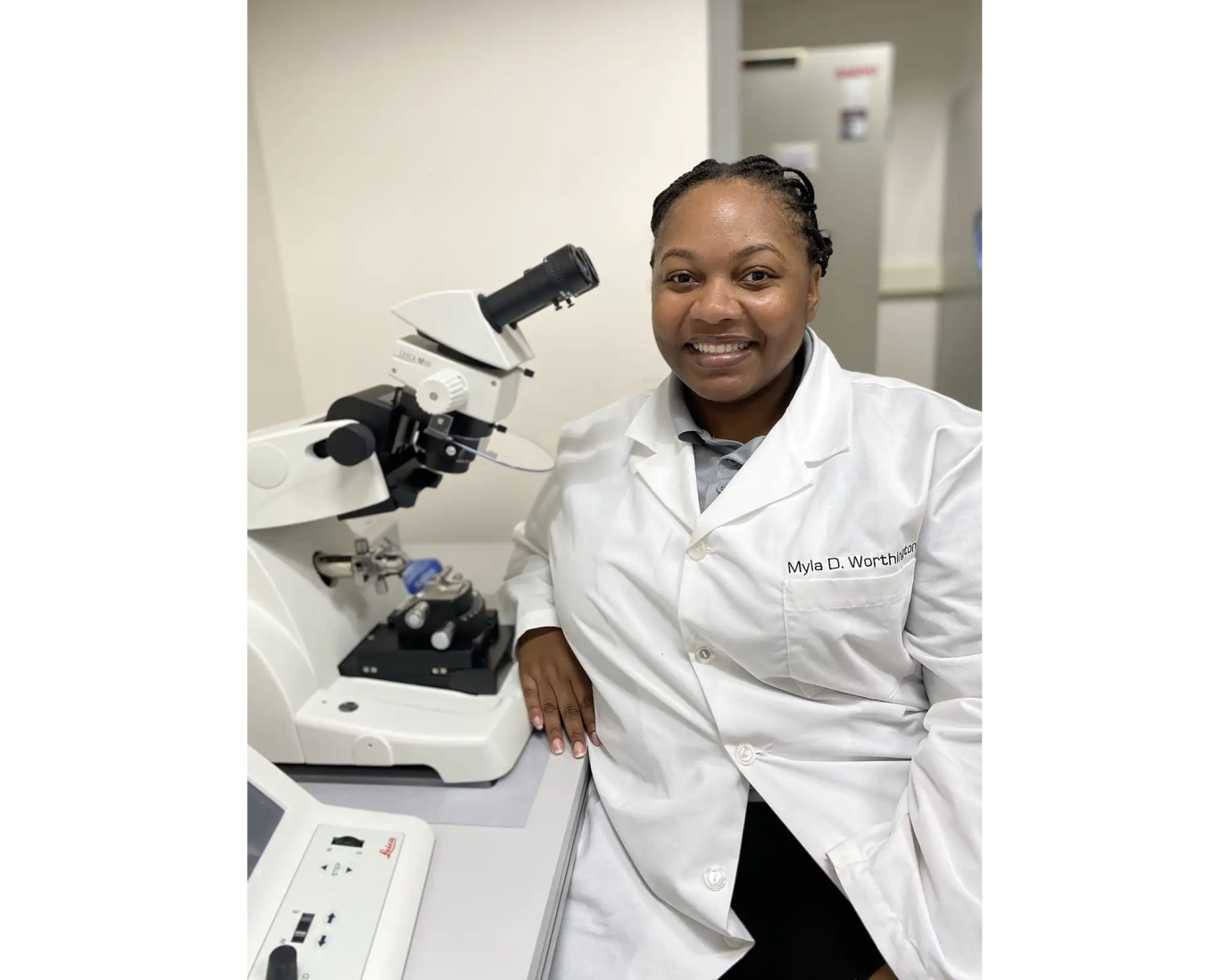 Myla Worthington in a white lab coat seated beside a microscope in a laboratory.