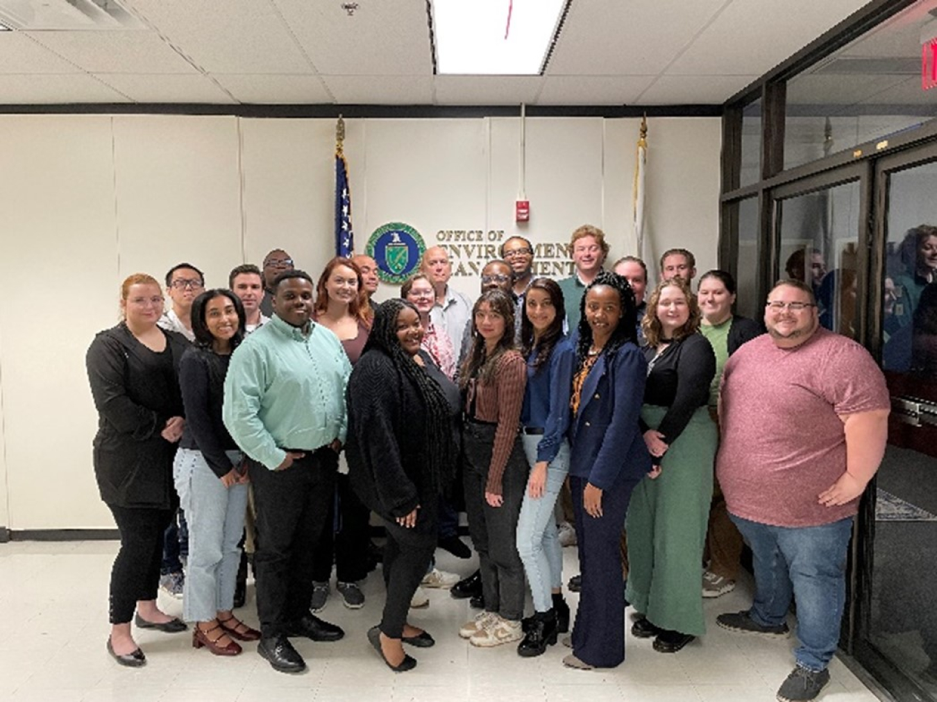 Group of 22 people standing in front of Office of Environmental Management sign on wall.