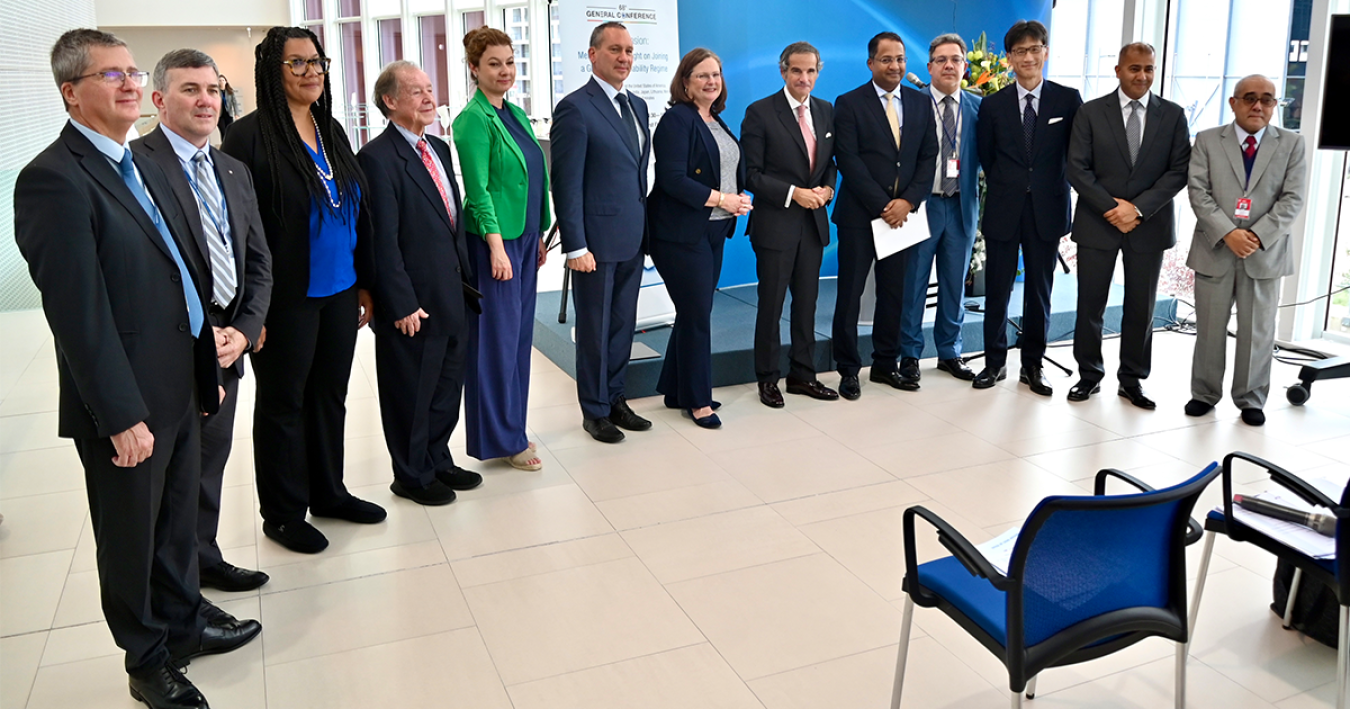 Group of men and women in business attire standing in an arc inside an office room, facing mostly toward the camera.