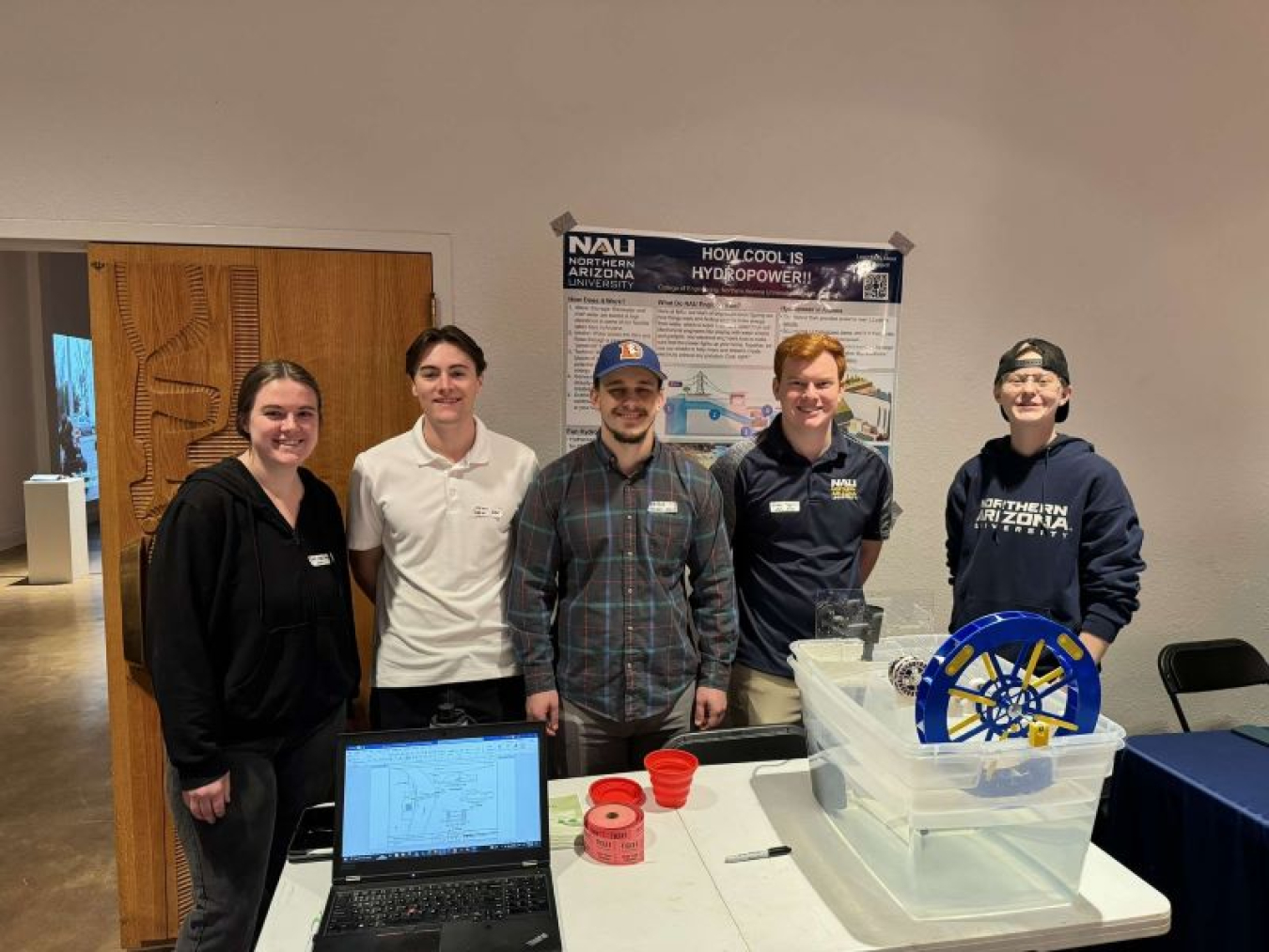 A photo containing five people, a computer, and a bucket of water.