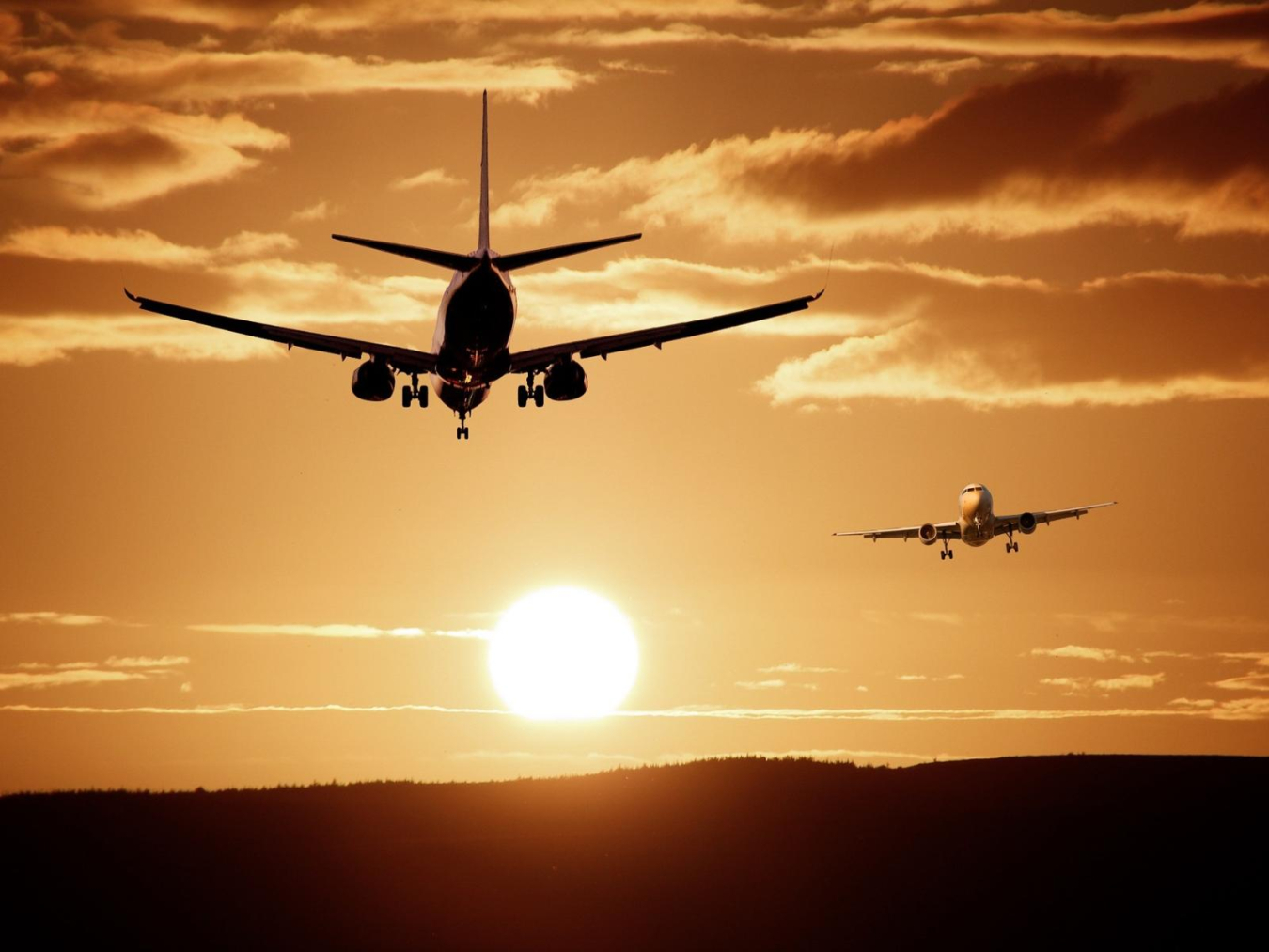 Two commercial jets flying in front of a sunset. 