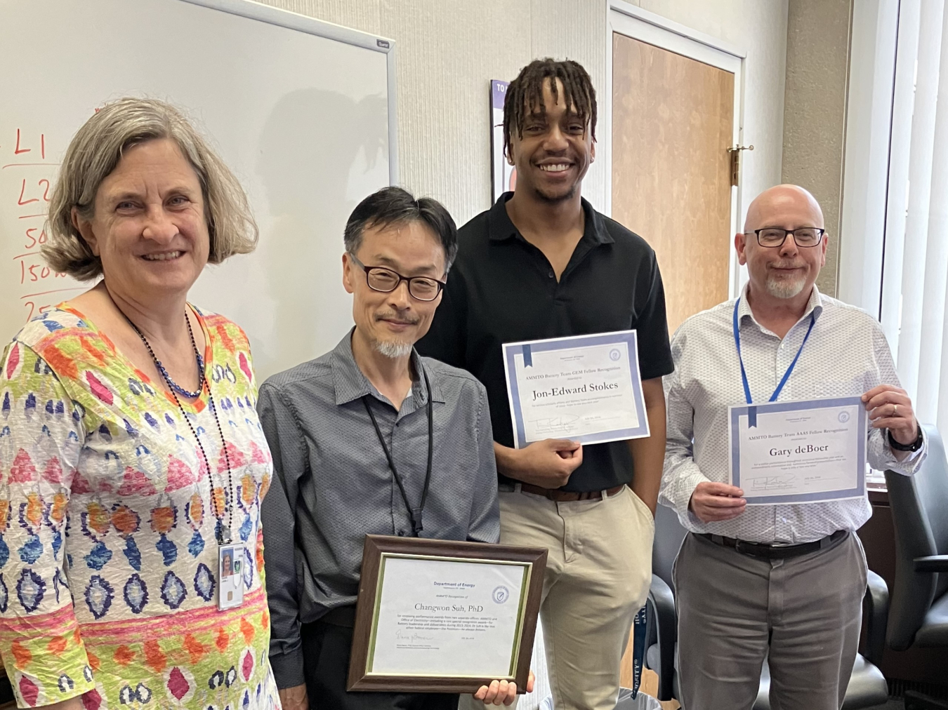 Stokes holding up a certificate while posing for a photo with three other people.