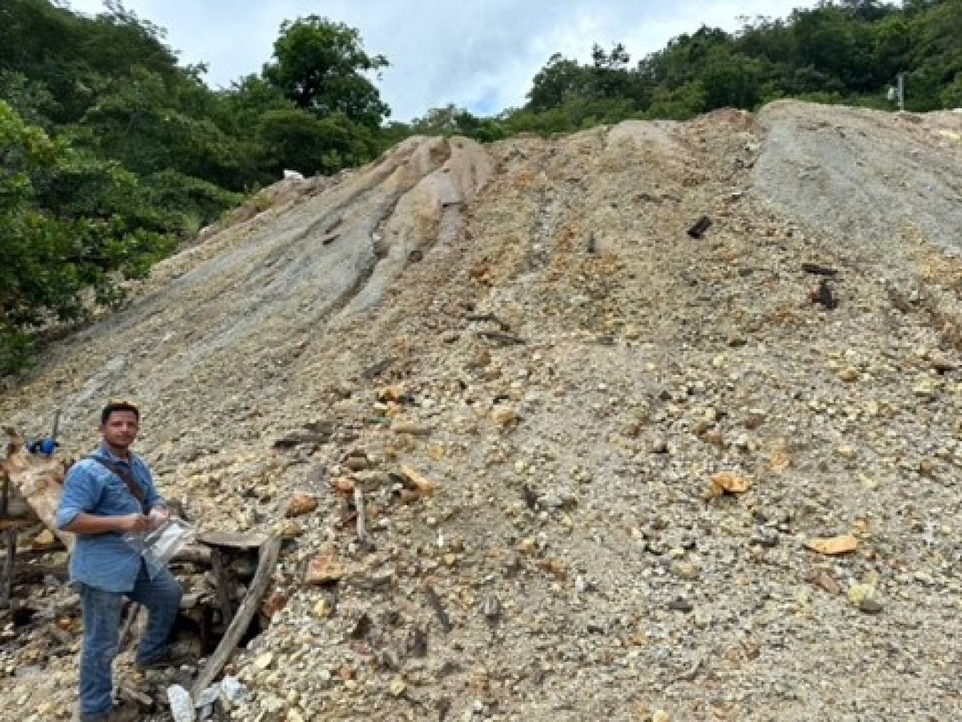 A man stands at the bottom of a pile of mining tailings. 