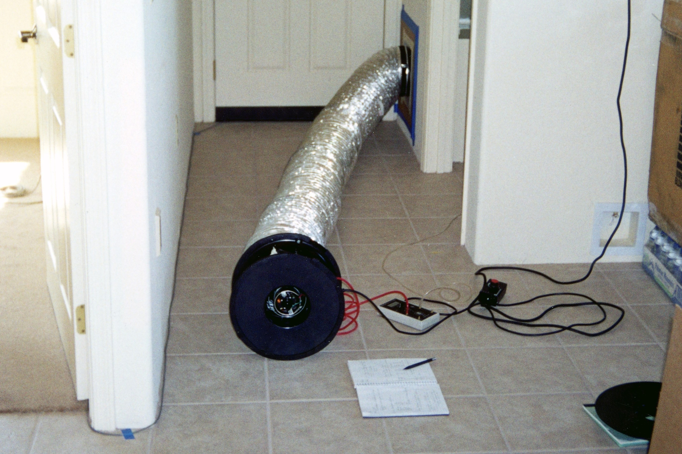 An air duct attached to cords and testing devices coming out of a wall in a hallway.