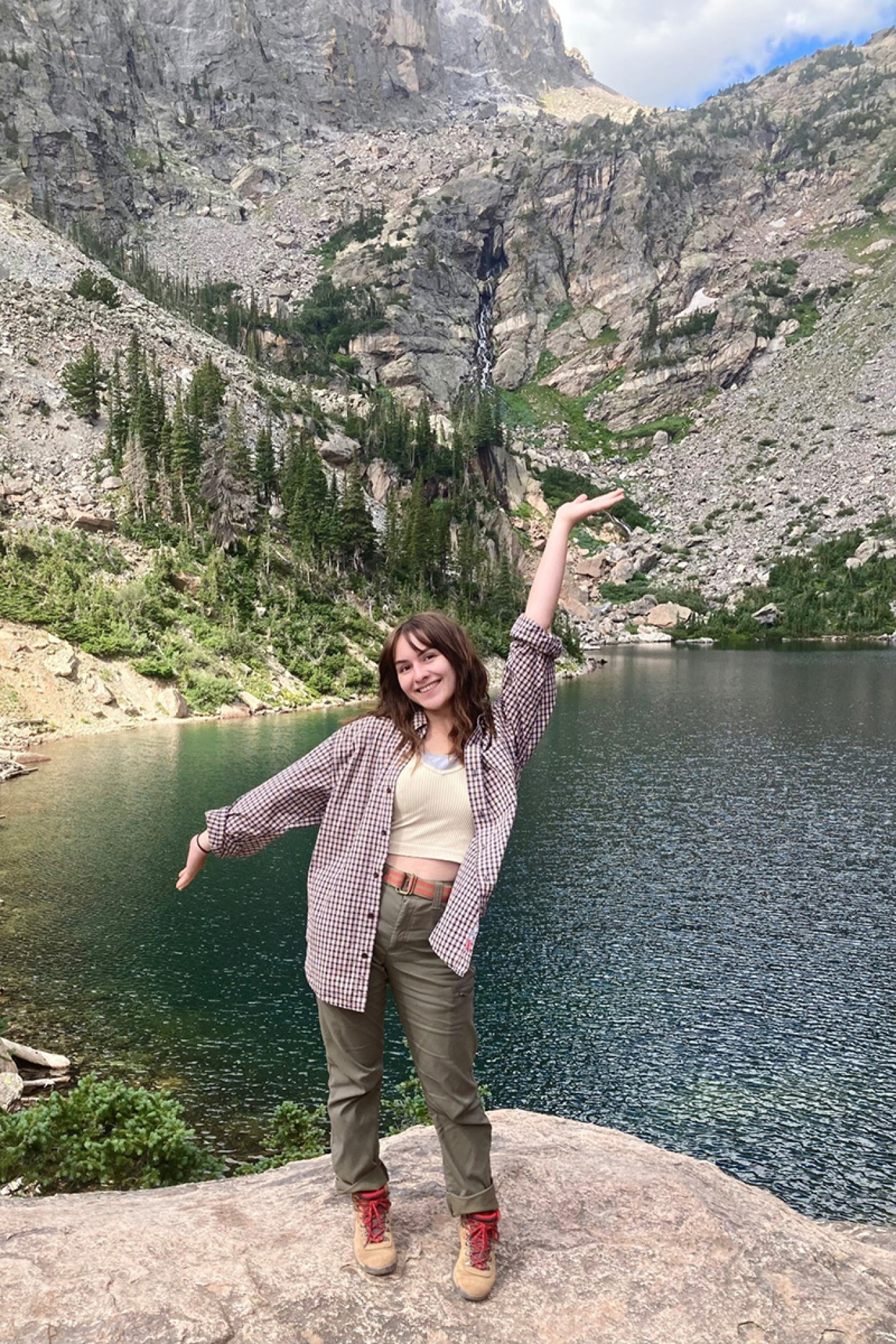 Person standing on rock with lake and rocky mountain in background.