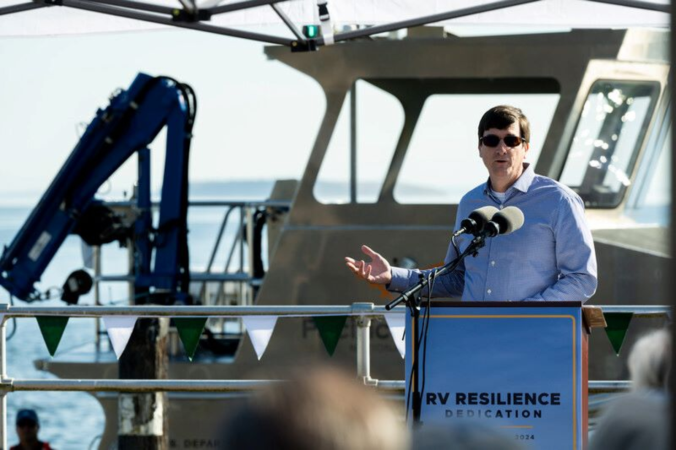 Matthew Grosso standing behind a podium on a platform near the ocean