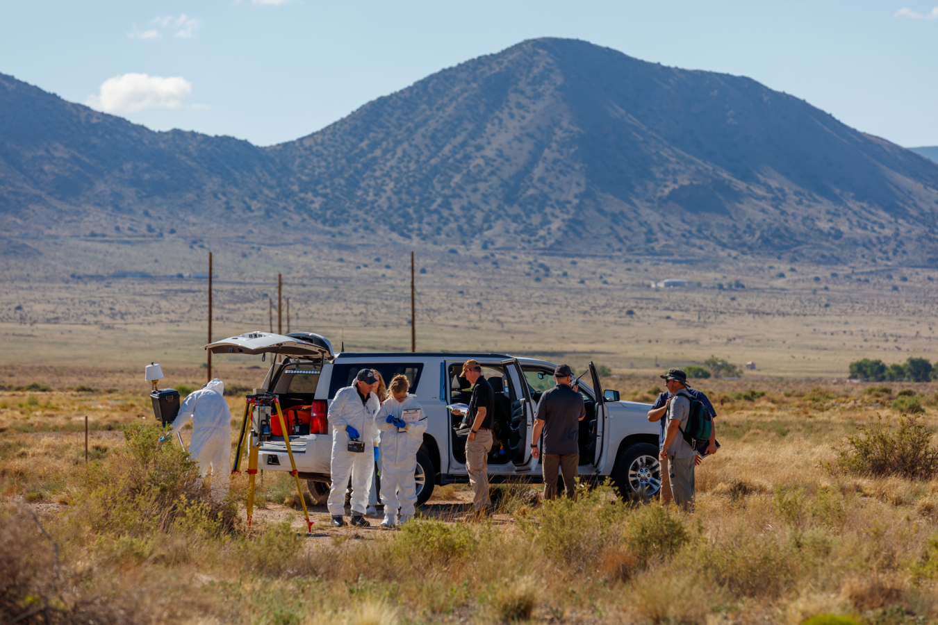 A group of technicians outside near a vehicle with a mountain in the background