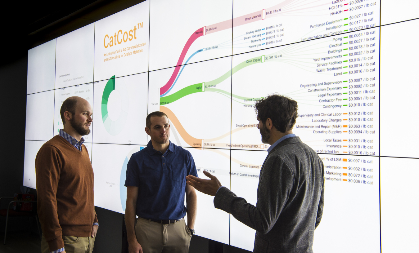 Three men infront of backlight screen of statistics