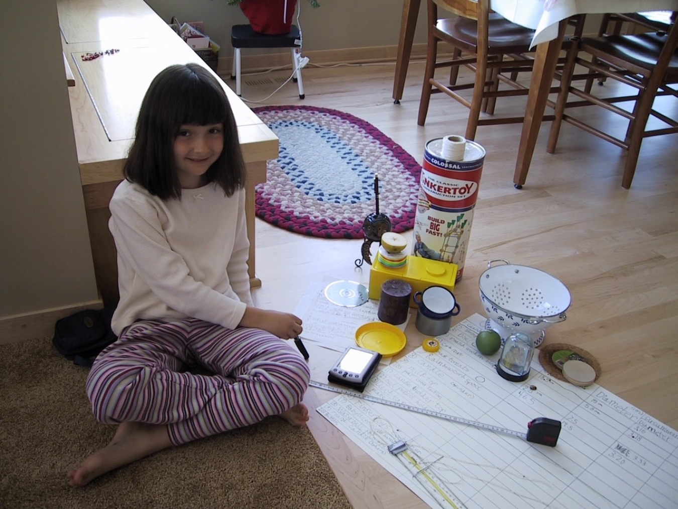 A young Emilie Lozier sits with a tape measure, a chart, a tinkertoy set, and other items to measure.