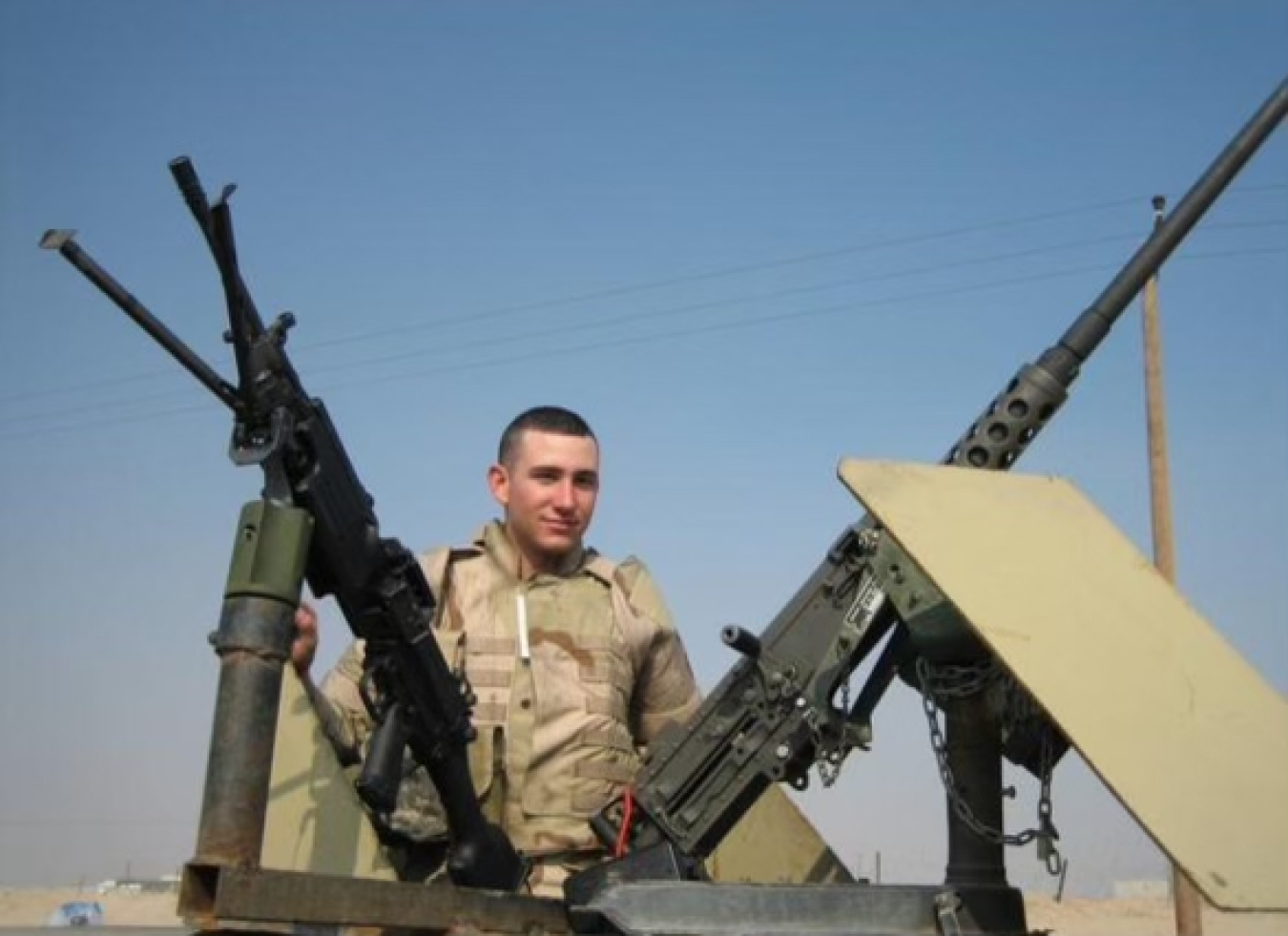 A man in a military uniform stands and poses for a picture between two large guns