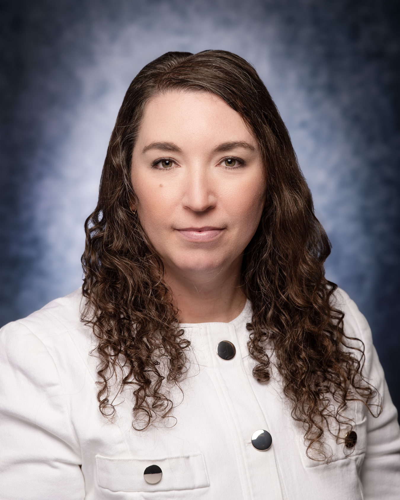 A professional headshot of a woman with shoulder length hair and a white button up jacket