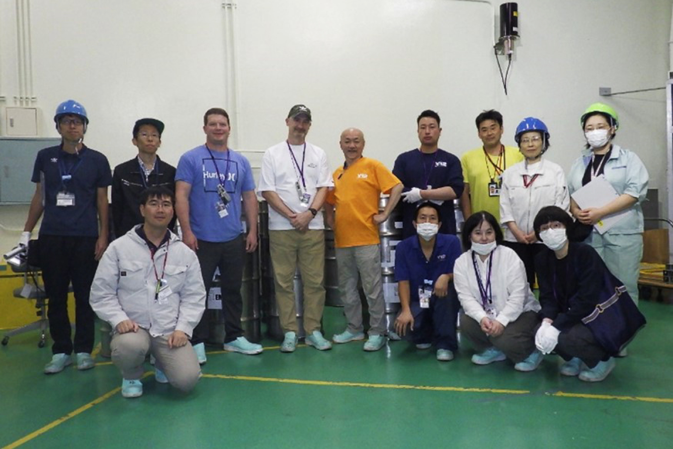 A group of about 20 people pose for a photo in a large indoor space. They are standing on a green, cement floor.