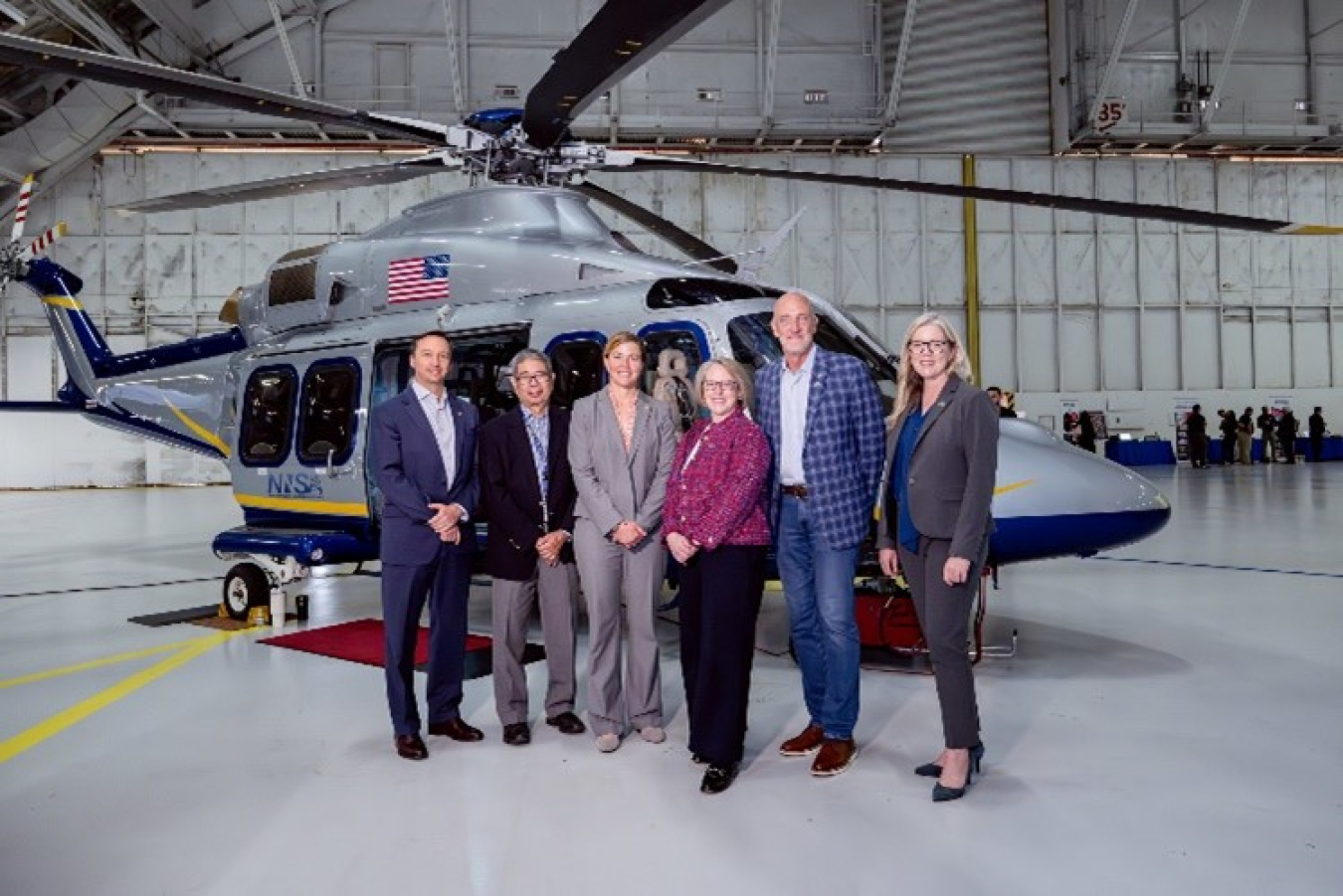 Six men and women stand in front of a NEST helicopter.