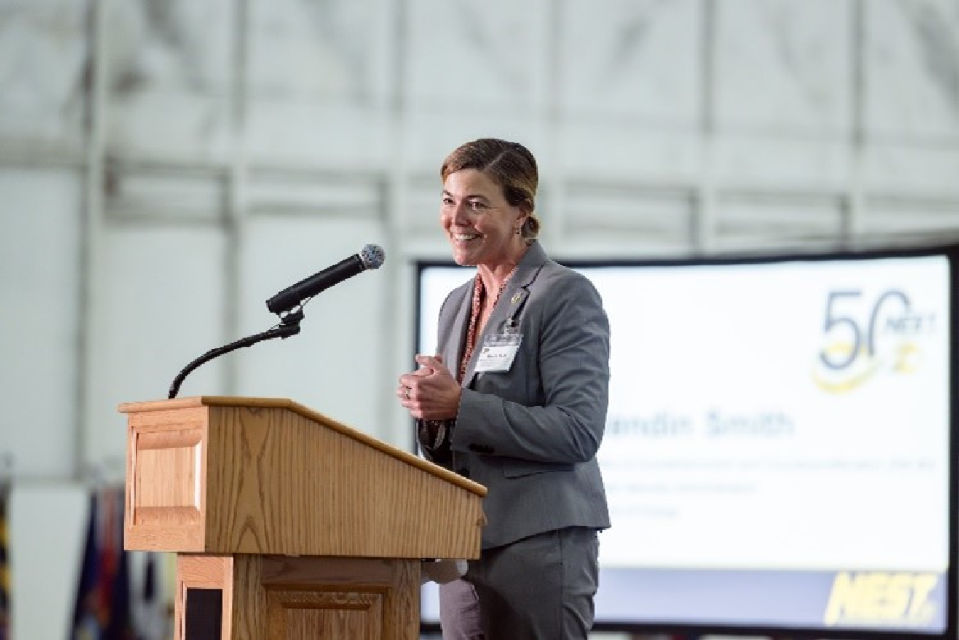 Dr. Wendin Smith speaks at a podium. A NEST aircraft is in the background.