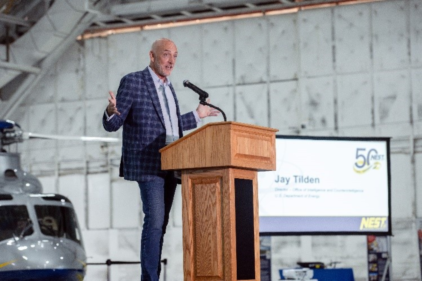 Jay Tilden speaks at a podium. A NEST aircraft is behind him.