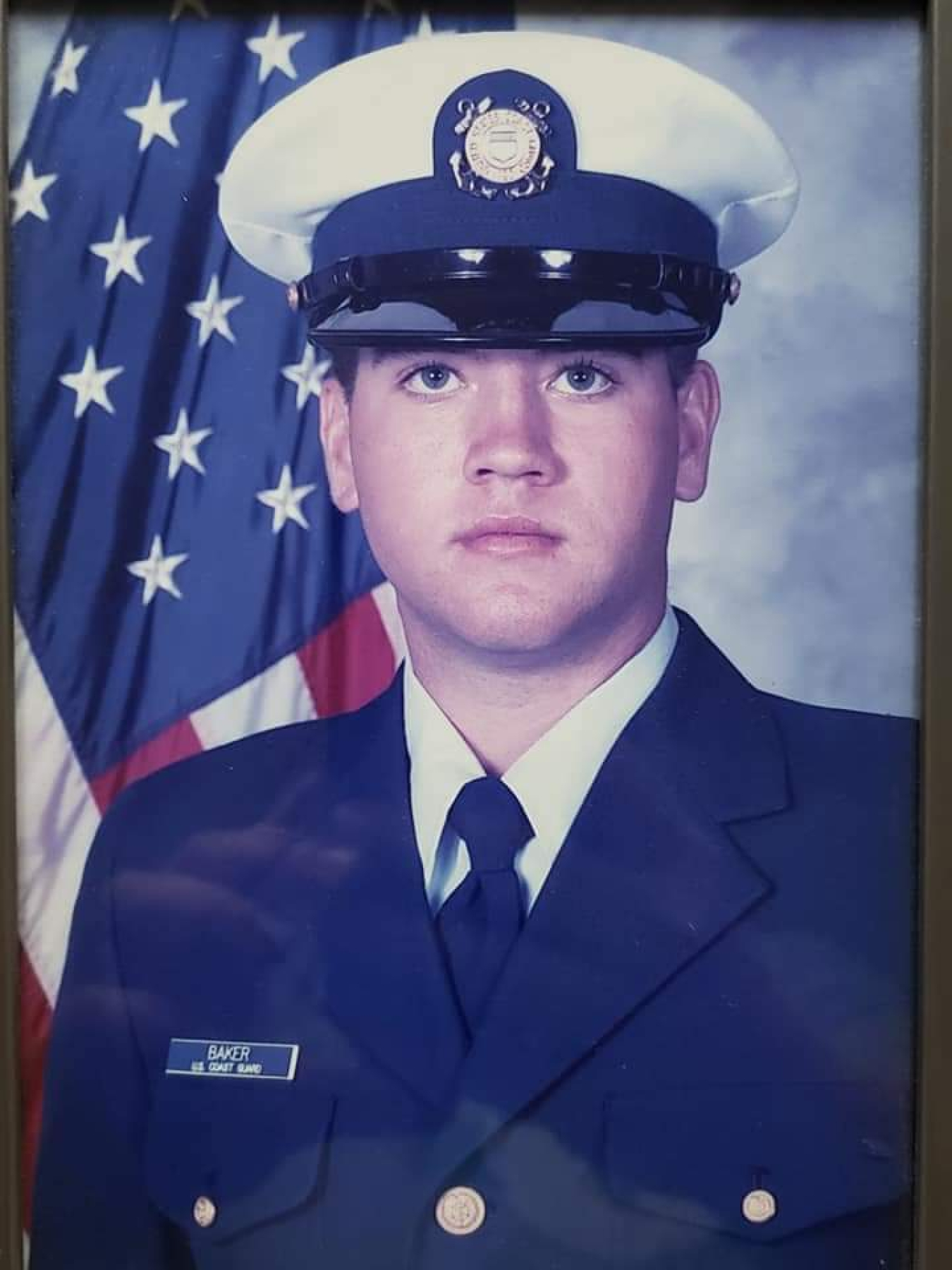 Photo of a person in military uniform infront of the American Flag.