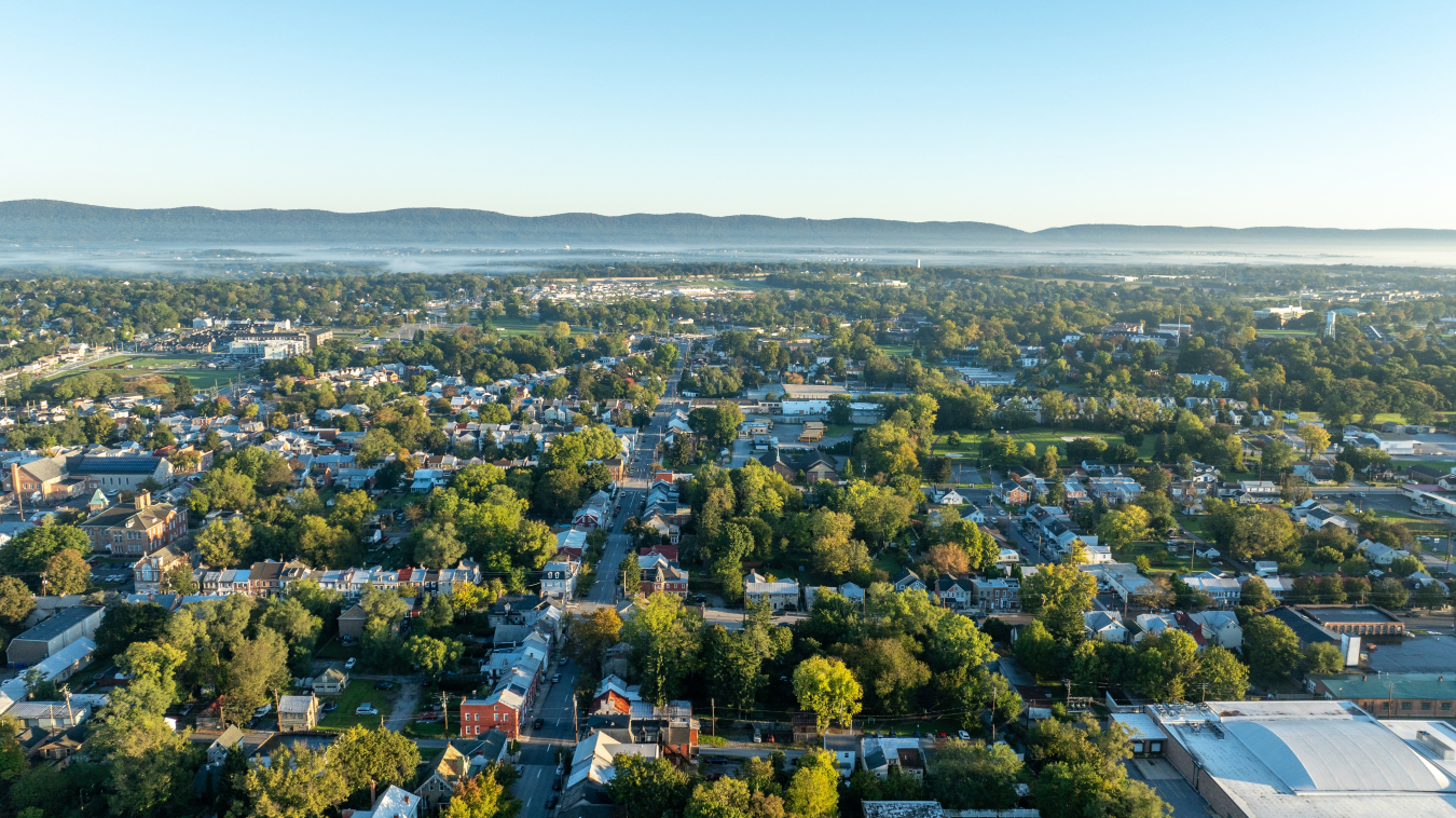 Overhead shot of a populous area, with trees interspersed with homes and other buildings, and mountains in the distance.