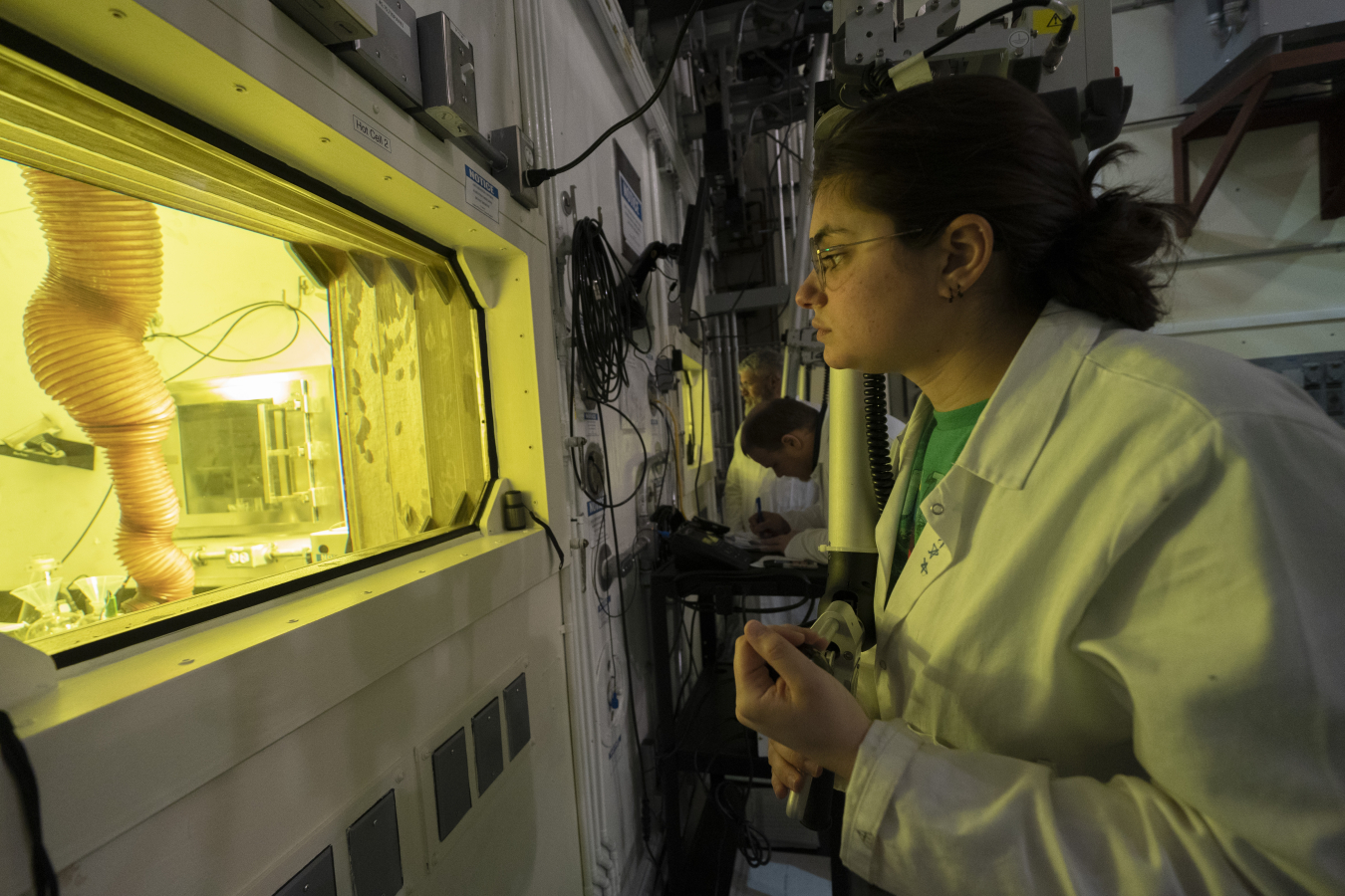 A woman looking into a window in a laboratory.