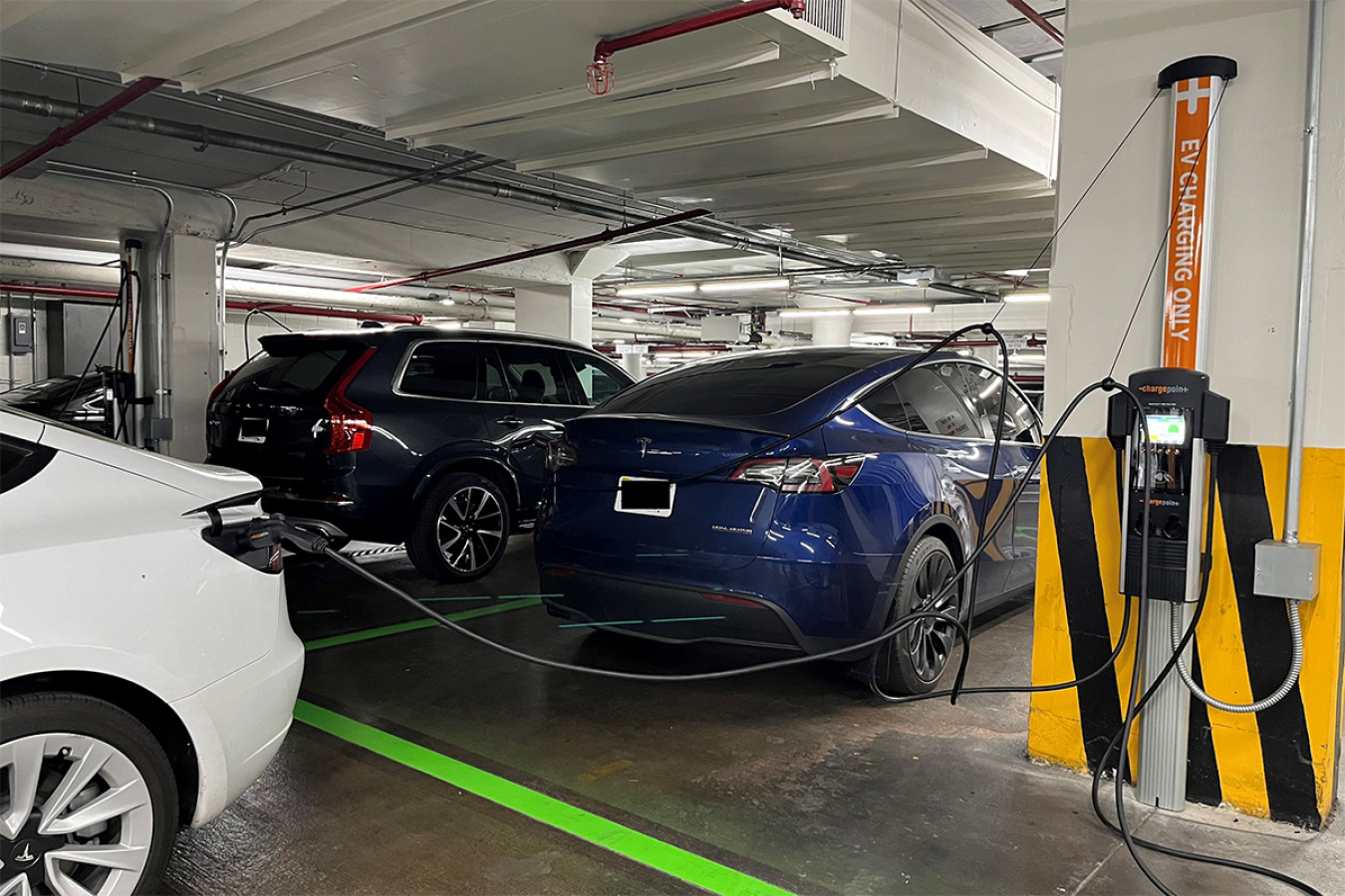 Electric vehicles plugged into a charging station in a parking garage.