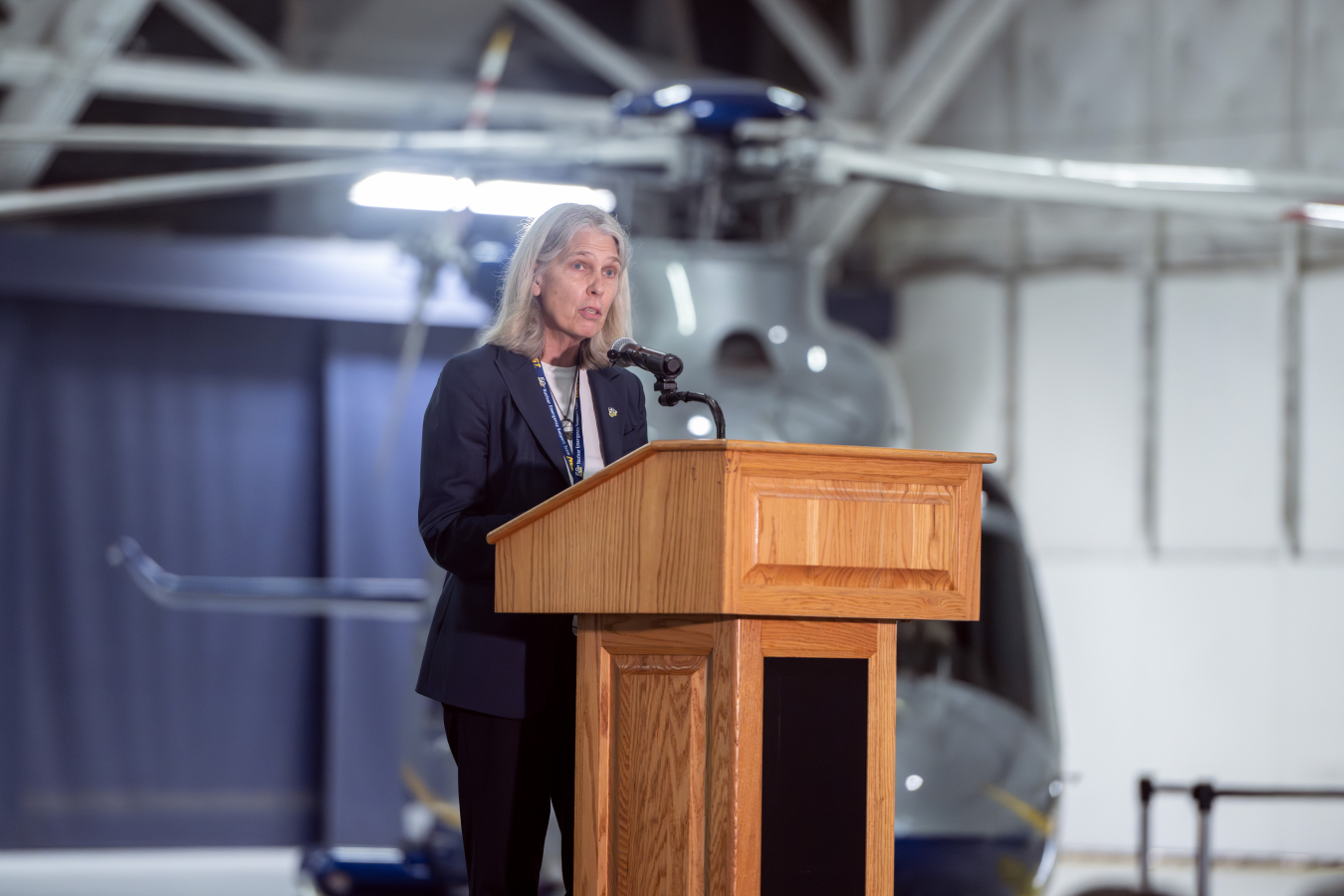 NNSA Administrator Hruby speaks at a podium with an aircraft behind her.