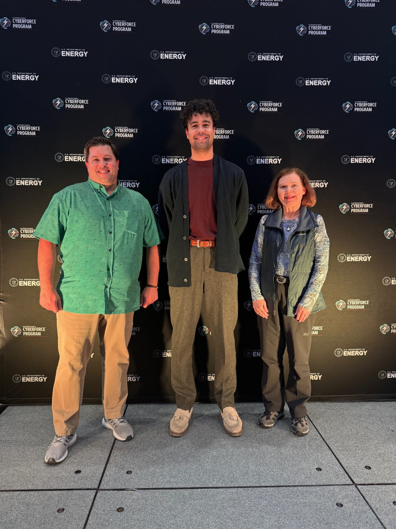 Three people stand against a backdrop of a wall of CyberForce branding.