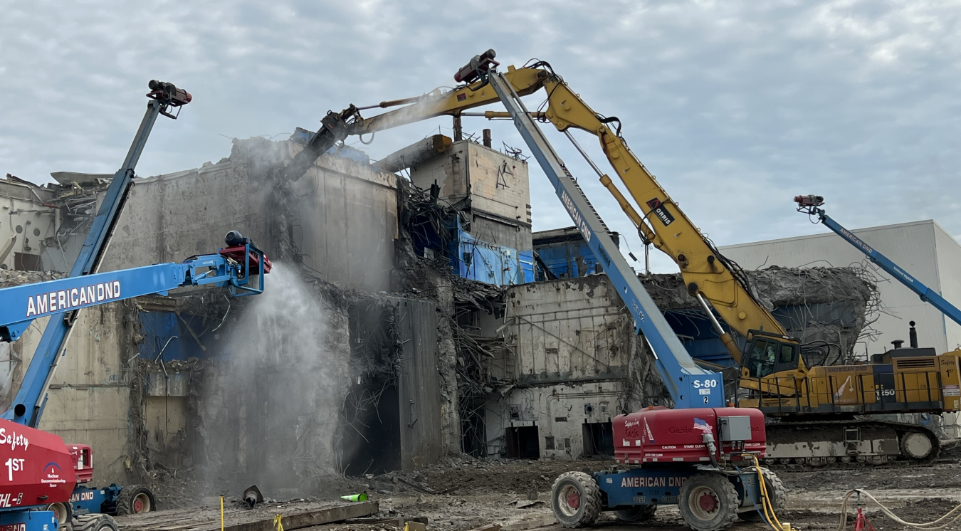 Heavy equipment, including multiple cranes, working to demolish a building