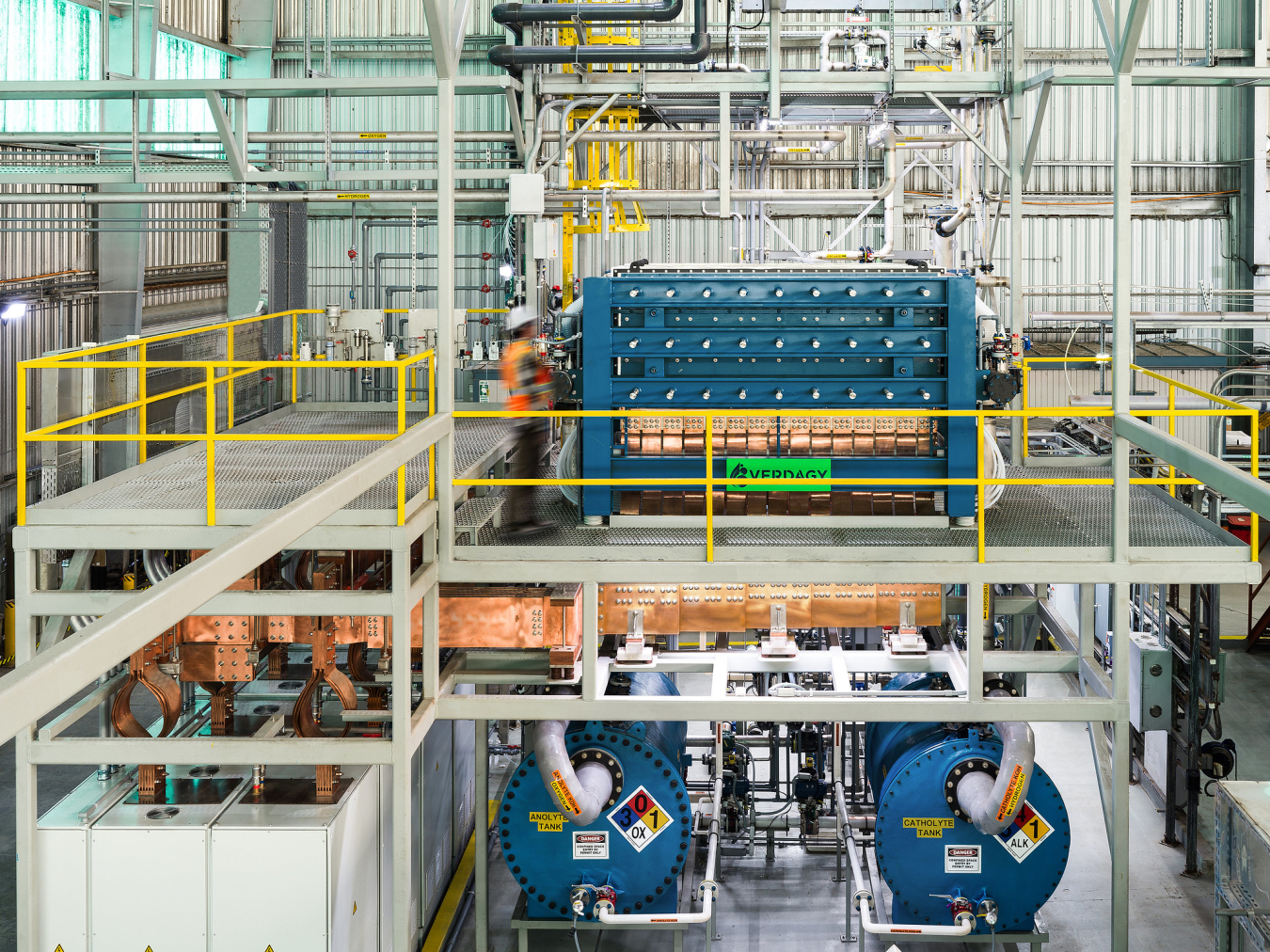 A worker in a hard hat and safety vest adjusts a machine in a factory setting.