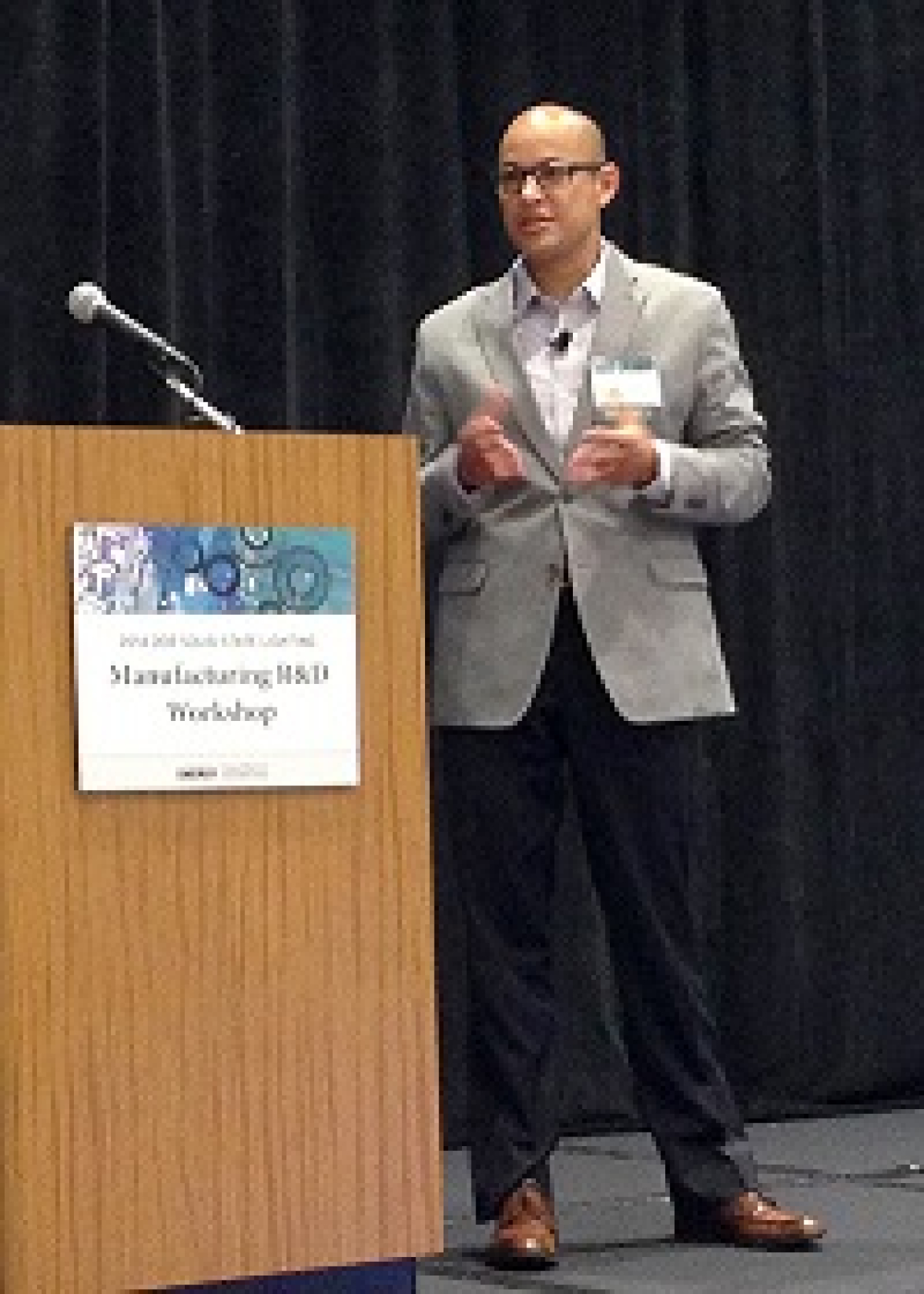 Man in a suit speaking next to a lectern, addressing the audience.