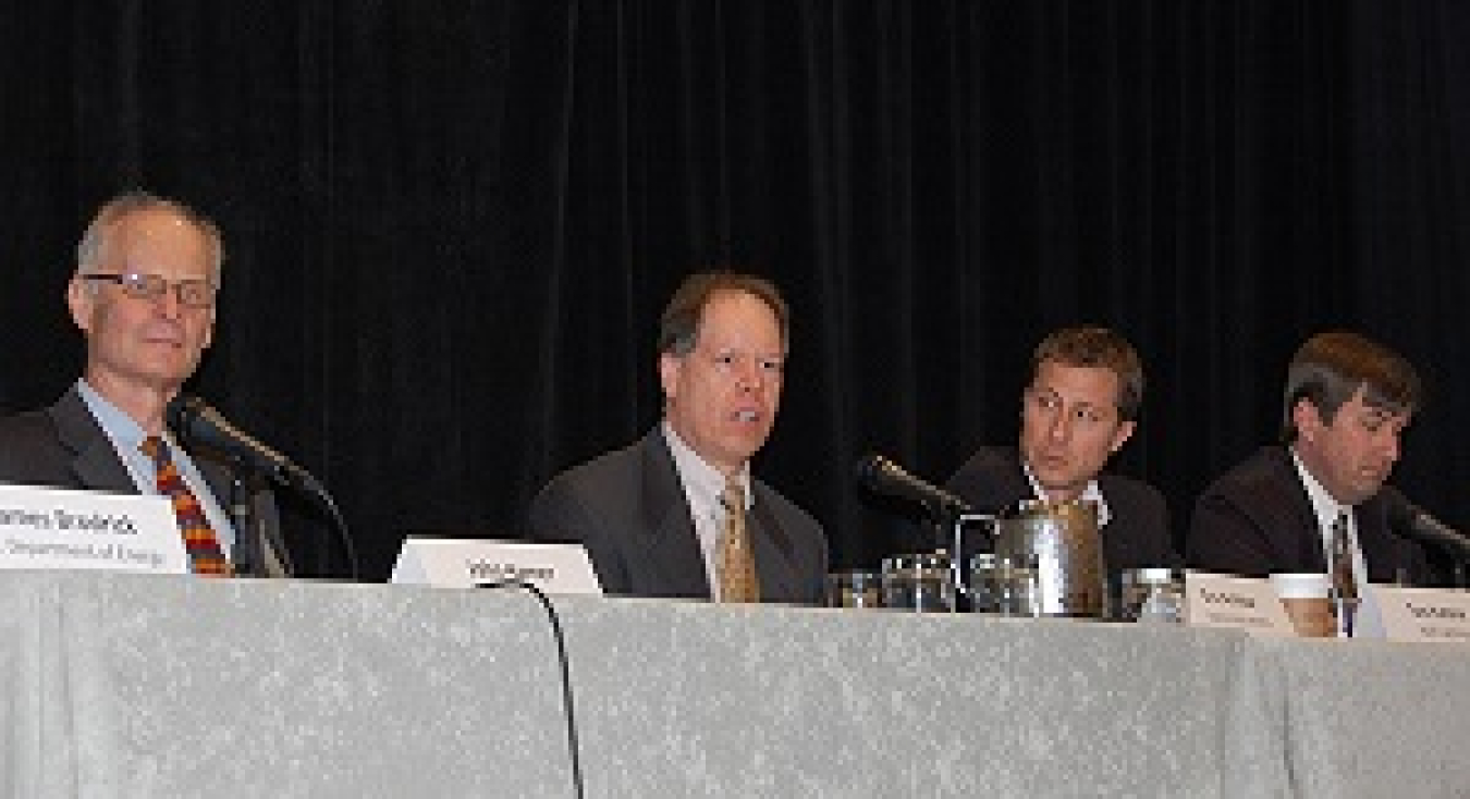 Photo of four men seated at a table, in front of microphones. One man is speaking into a microphone, answering a question.