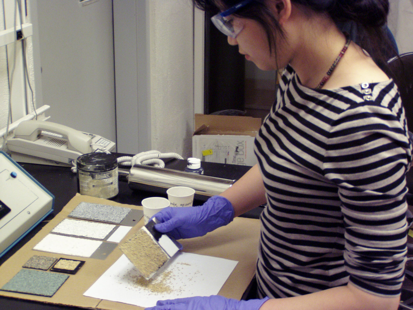 Photo of a woman standing at a table looking at different kinds of shingle materials.