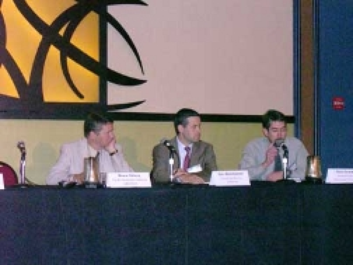 A photo of three panelists seated at a table and addressing the audience.