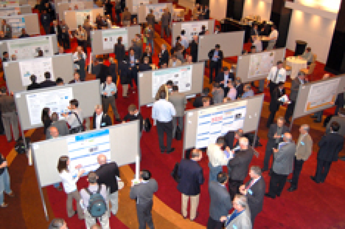 Photo showing an aerial view of a workshop poster session, with clusters of people gathered around posters and talking.