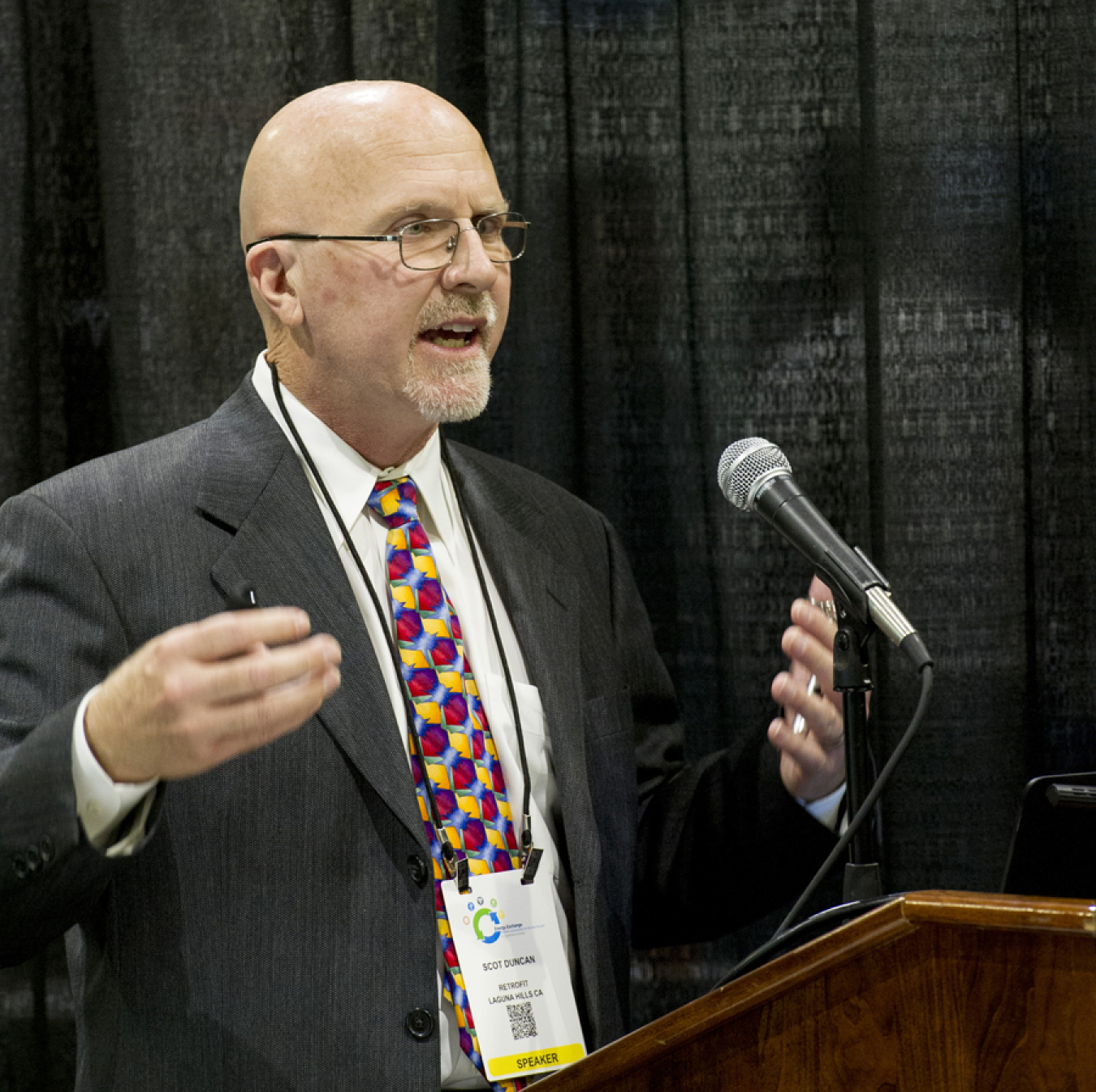 Man in a business suit speaking at a microphone.