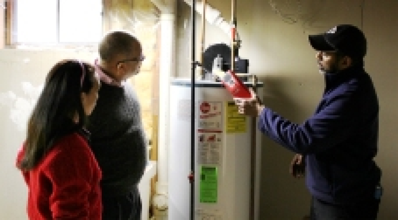 A person examining a hot water heater while another person stands nearby.