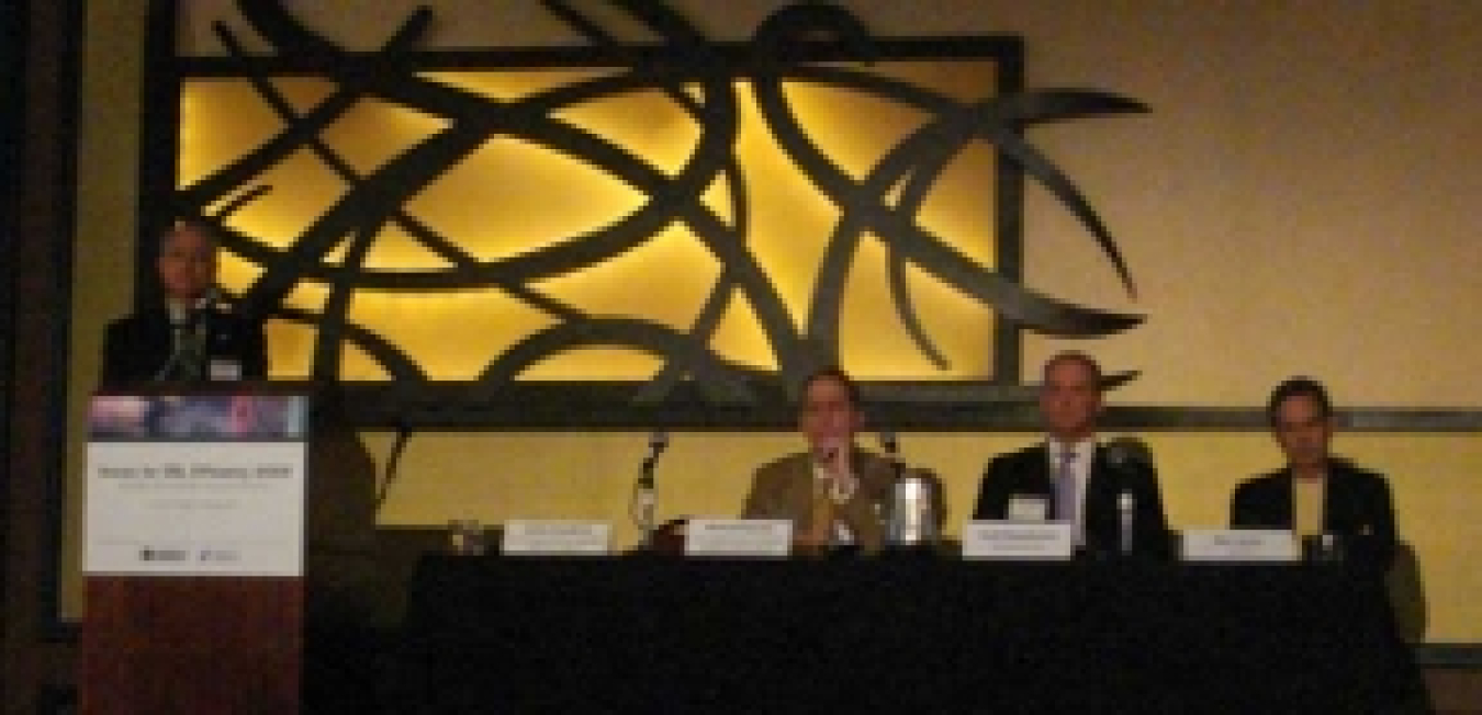 A photo of three panelists sitting while a moderator stands at a podium.