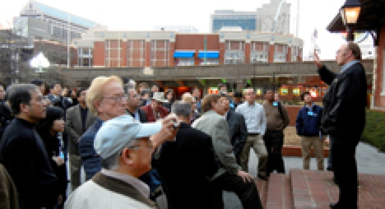 Photo of a large group of people standing outside of a city building, listening to a man speak on the building's steps.