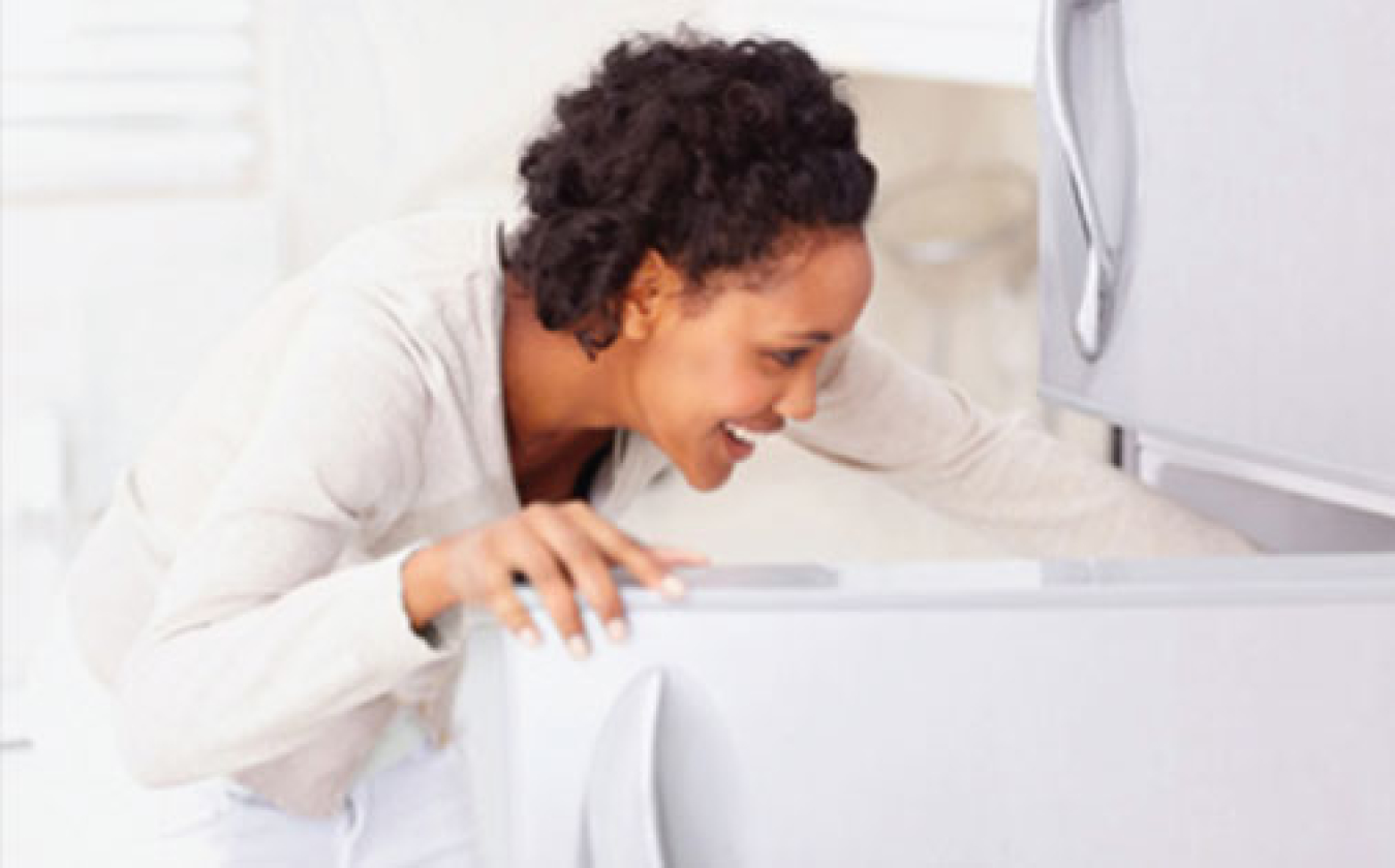 Photo of a woman smiling as she gets something out of the refrigerator.